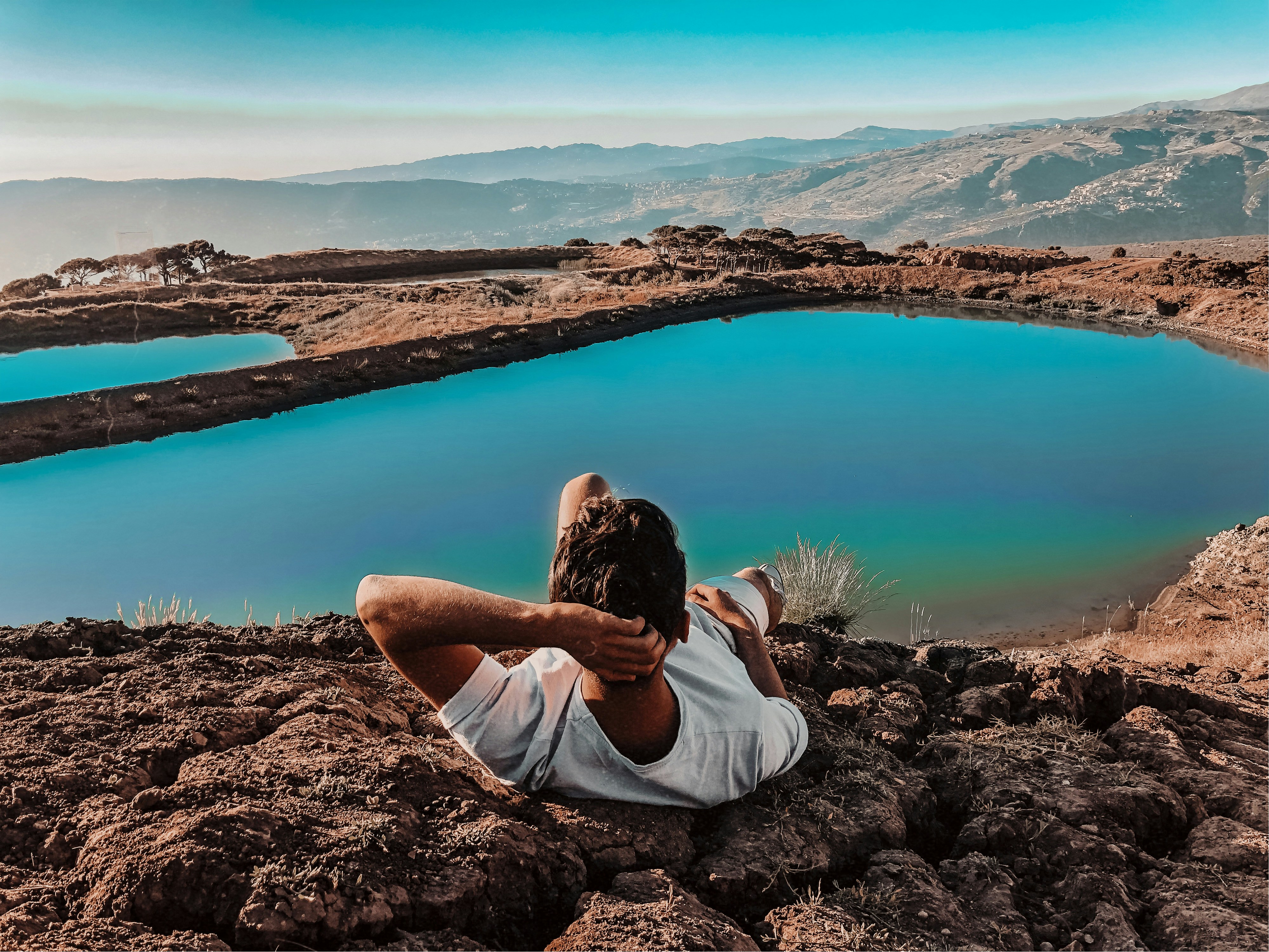 woman in white shirt sitting on brown rock near lake during daytime