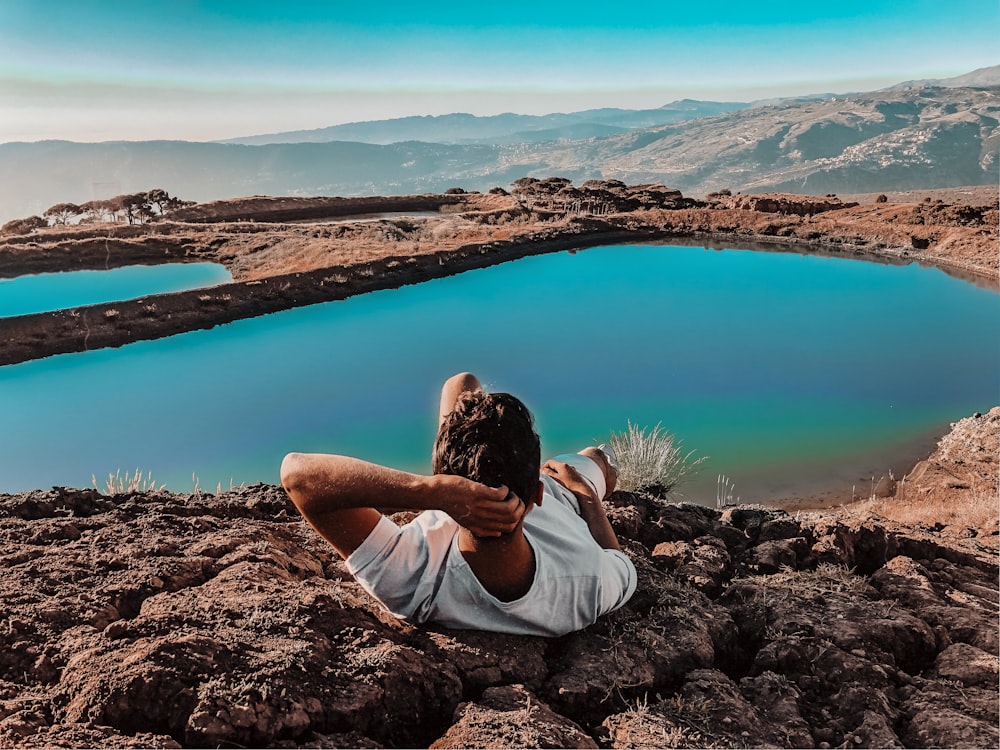 woman in white shirt sitting on brown rock near lake during daytime