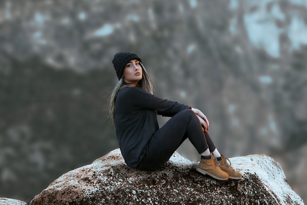 woman in black jacket and black pants sitting on rock
