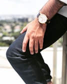 A man adjusting his miharo watch while seated at a café, with blurred urban background.