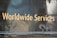 Golden text displaying 'Worldwide Services' is set against a dark, reflective surface, likely part of a vehicle or metallic structure, featuring rivets and a slightly worn texture.