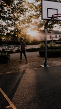 A mentor and a young person talking while walking on a basketball court at sunset.