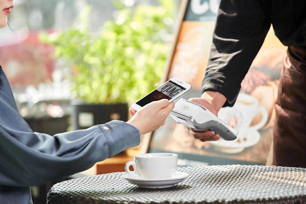 person holding white ceramic mug and black smartphone