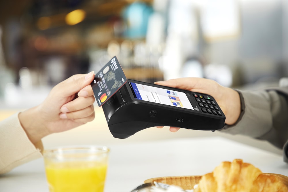 person holding black smartphone near clear drinking glass