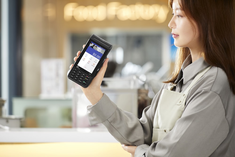 woman in gray coat holding black smartphone