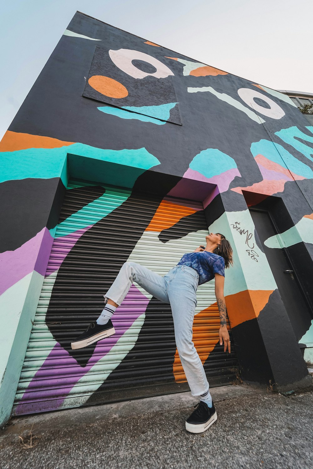 woman in blue denim jacket and white pants standing on wall with graffiti during daytime