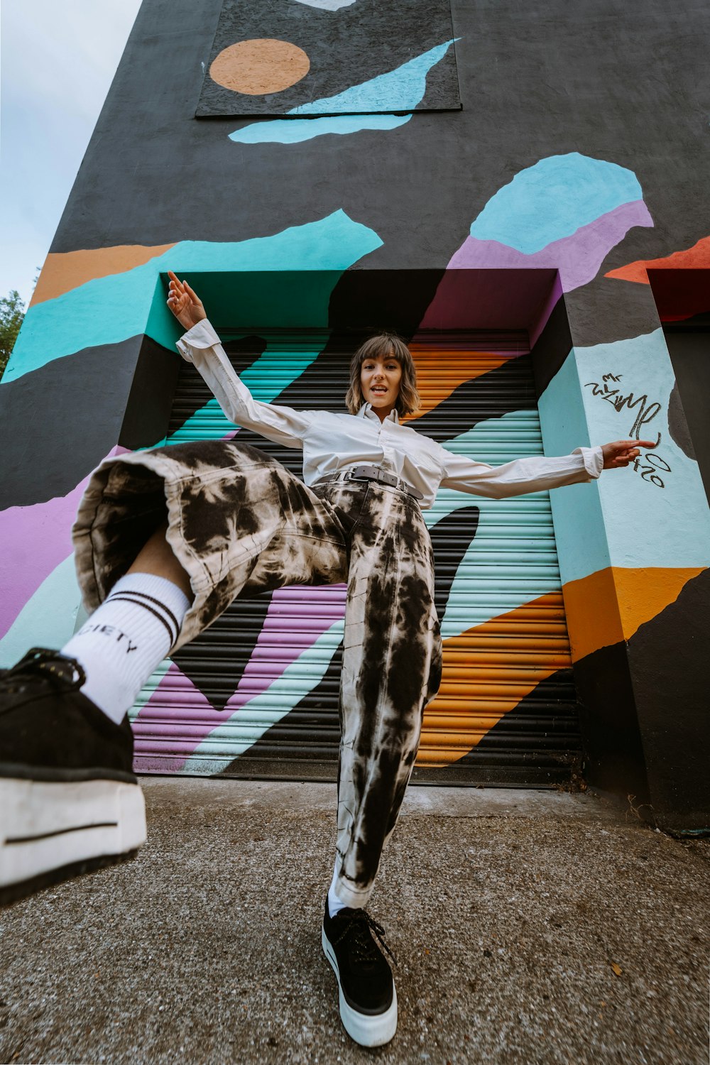 woman in white shirt and black pants sitting on concrete wall with graffiti