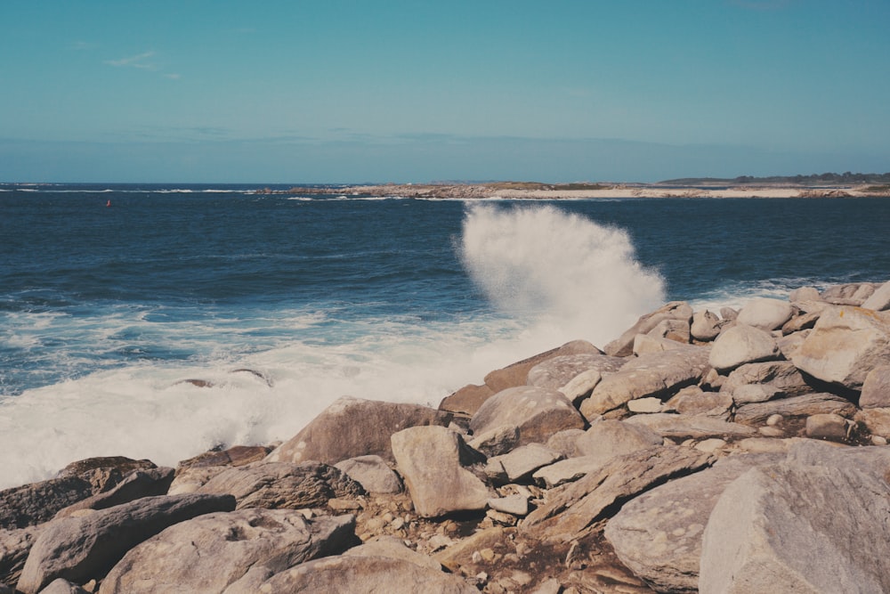costa rochosa marrom com ondas do oceano sob o céu azul durante o dia