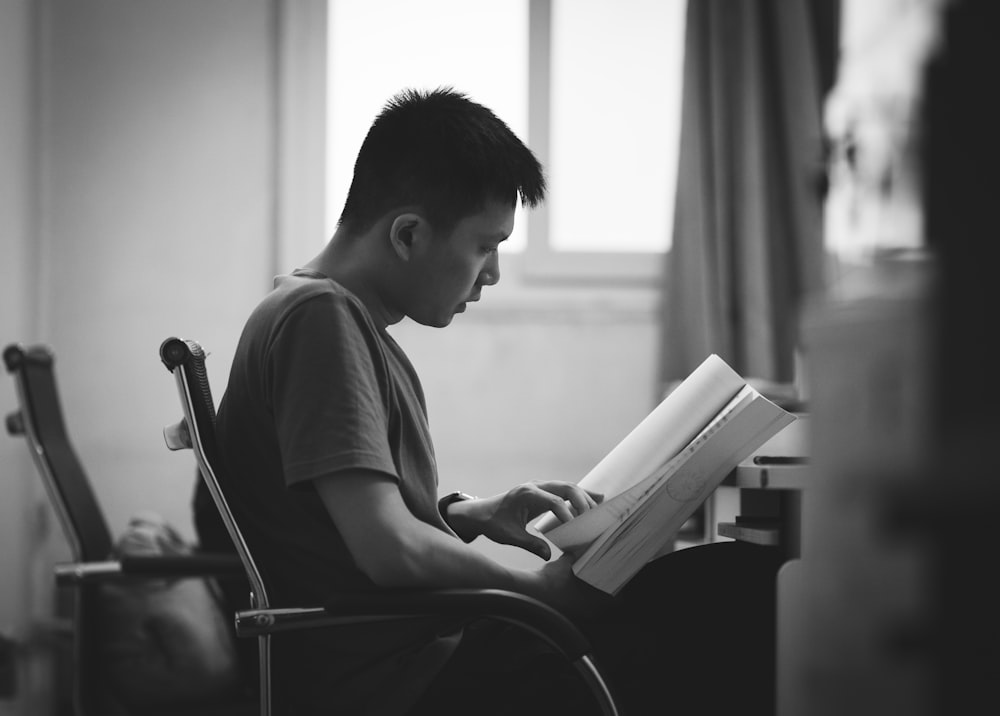 grayscale photo of man reading book