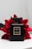 A sleek black perfume bottle labeled Coco Noir Chanel Paris is positioned against a backdrop of vibrant red flowers. The bottle's simplistic design and gold accents exude luxury and elegance. The contrast between the dark bottle and the bright flowers creates a striking visual appeal.
