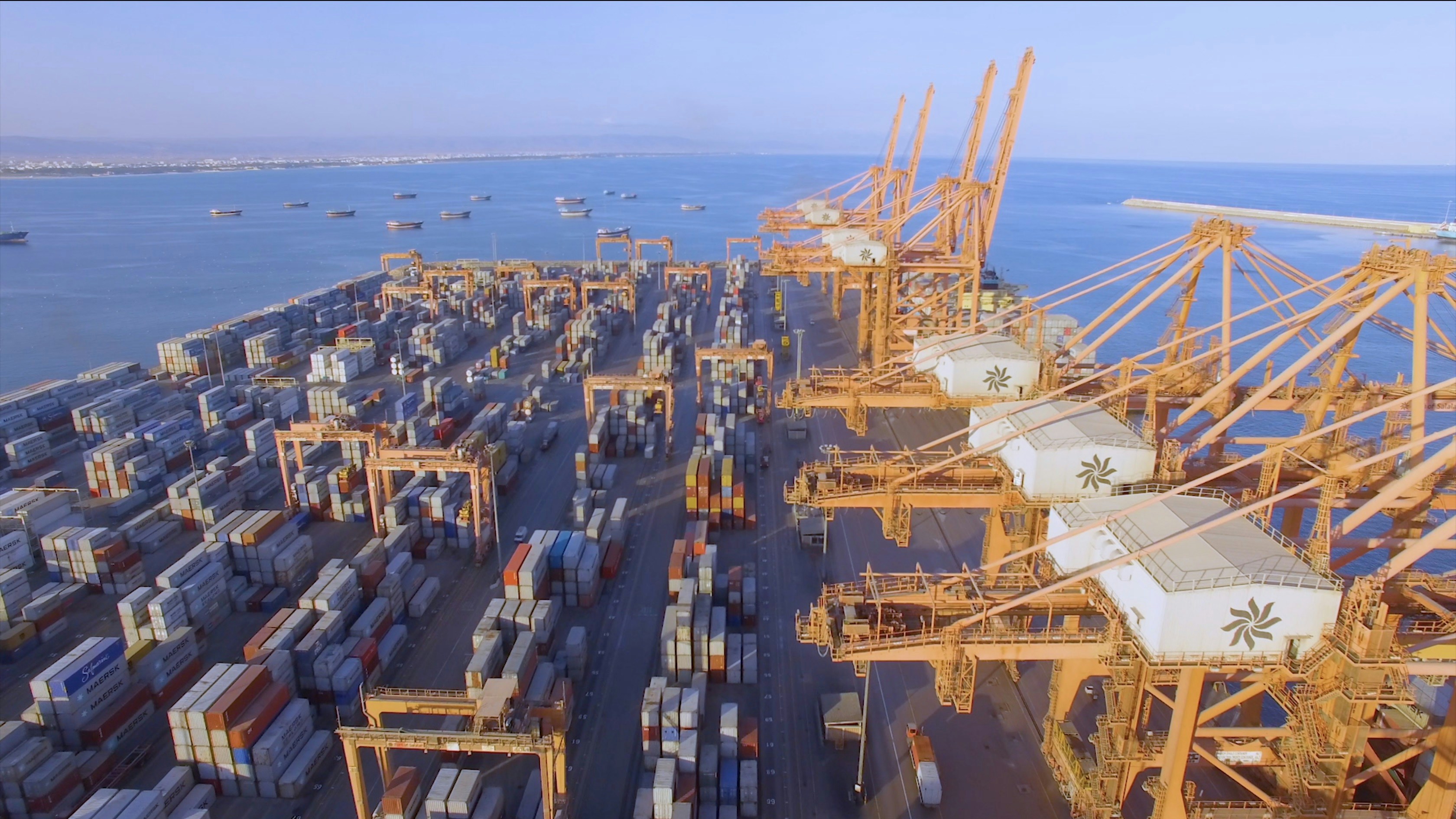 Busy international shipping port with large container cranes, stacked colourful containers, aerial view, golden hour