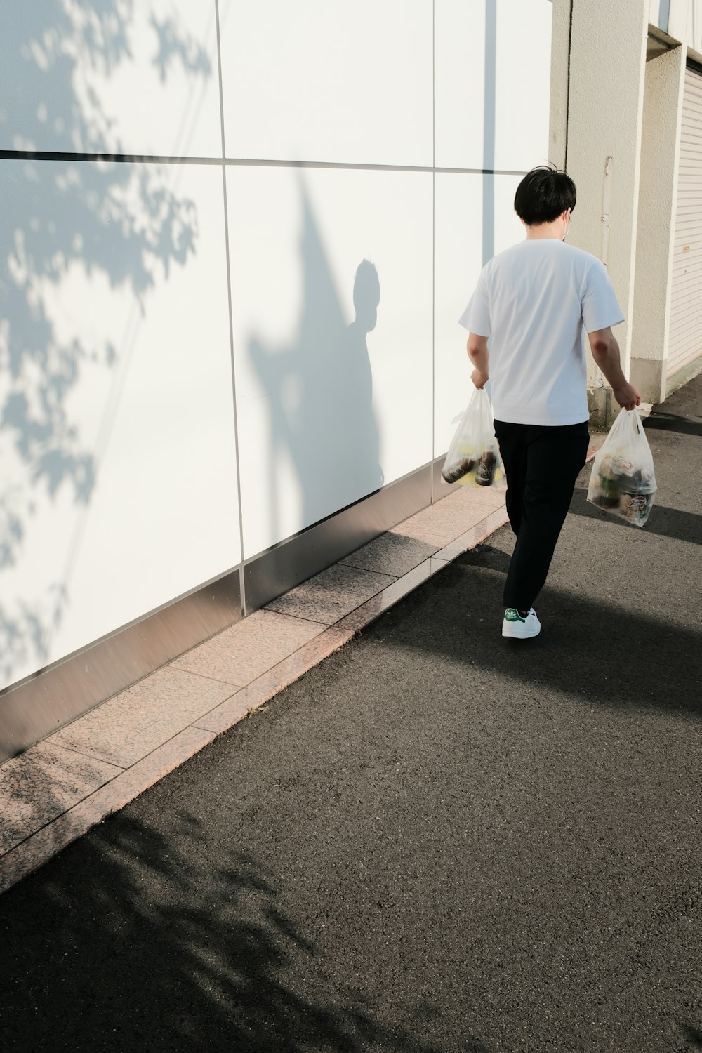 homem de camiseta branca e calças pretas andando na calçada de concreto cinza