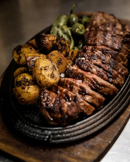 A vibrant platter featuring various cuts of grilled beef, set against a backdrop of red and white checkered cloth.