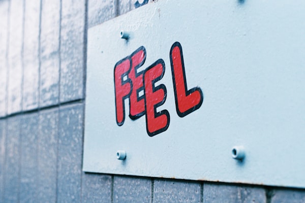 a white metal sign on a wall with the word "feel" in red letters outlined in black