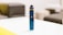 A blue electronic vaping device is placed on a white table in a room with blurred background furniture.