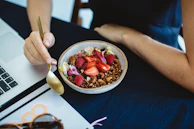 Hand holding a golden spoon over a bowl of vibrant salad with fresh herbs and nuts.