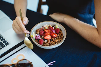 Hand holding a golden spoon over a bowl of vibrant salad with fresh herbs and nuts.