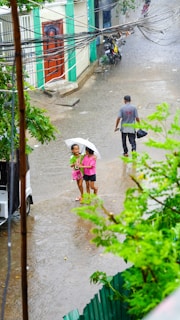2 boys walking on sidewalk holding umbrella during daytime