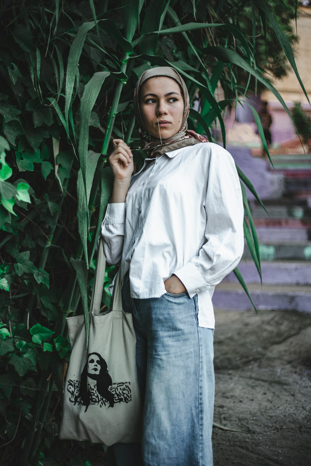 Mujer con camisa blanca de manga larga y jeans de mezclilla azul de pie junto a plantas verdes durante el día