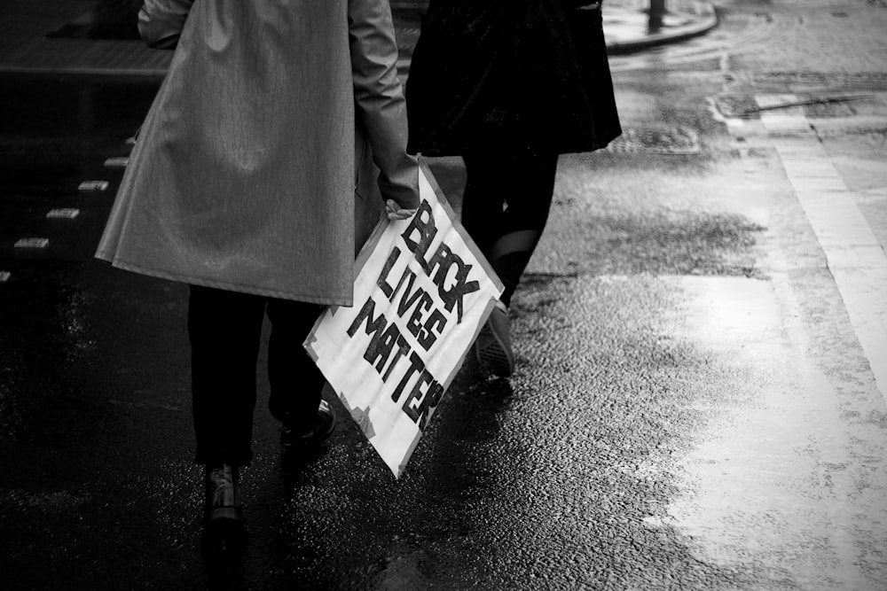 grayscale photo of person holding white and blue no smoking sign