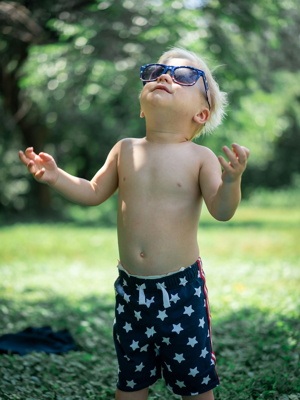 topless boy wearing blue and white floral shorts and black sunglasses