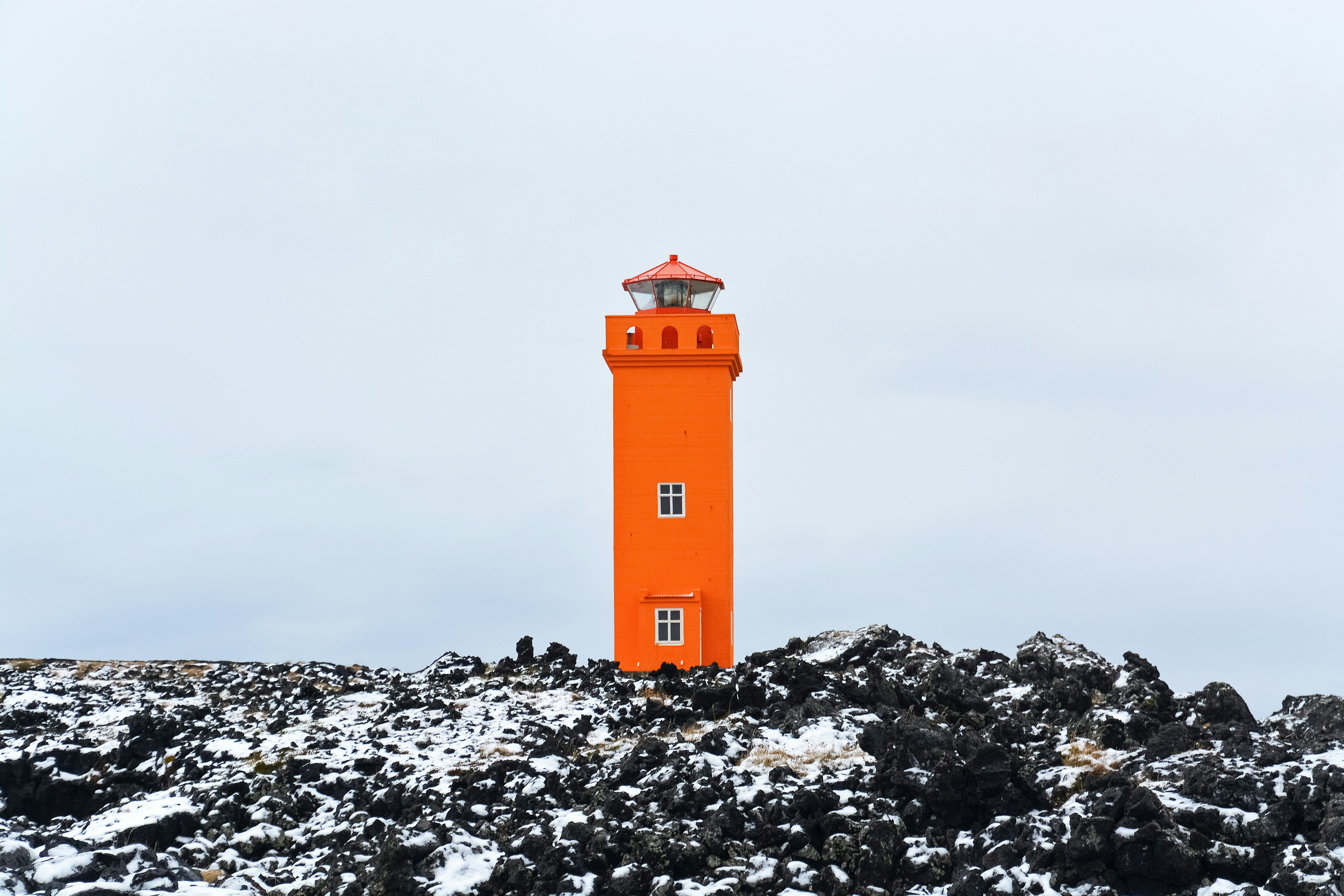 orange and white lighthouse on rocky ground under gray sky