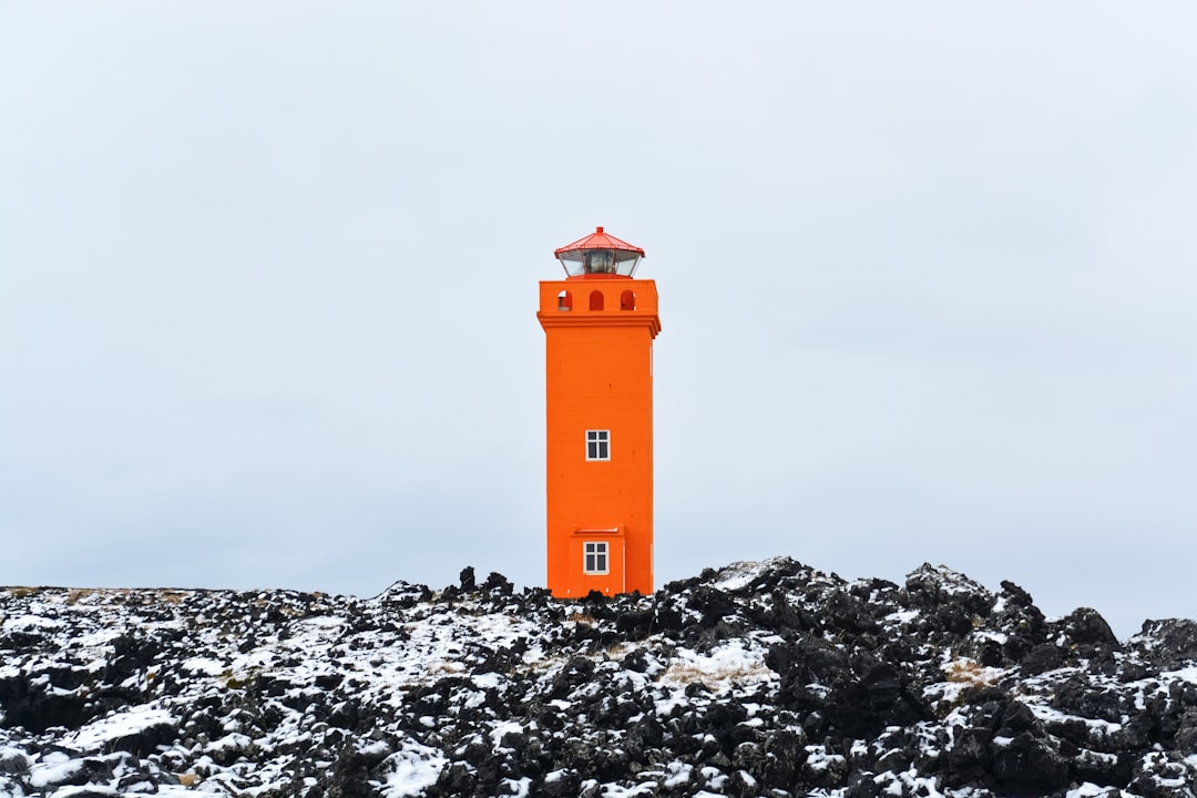 orange and white lighthouse on rocky ground under gray sky