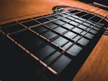 Close-up of a vintage acoustic guitar with warm brown and orange tones on a black background, featuring subtle parallax movement.