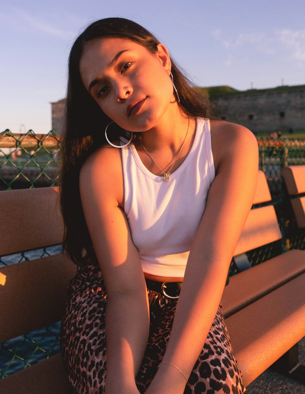 woman in white tank top and black and white leopard pants sitting on brown wooden bench