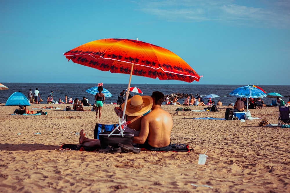 man sitting on blue and white chair under orange umbrella on beach during daytime