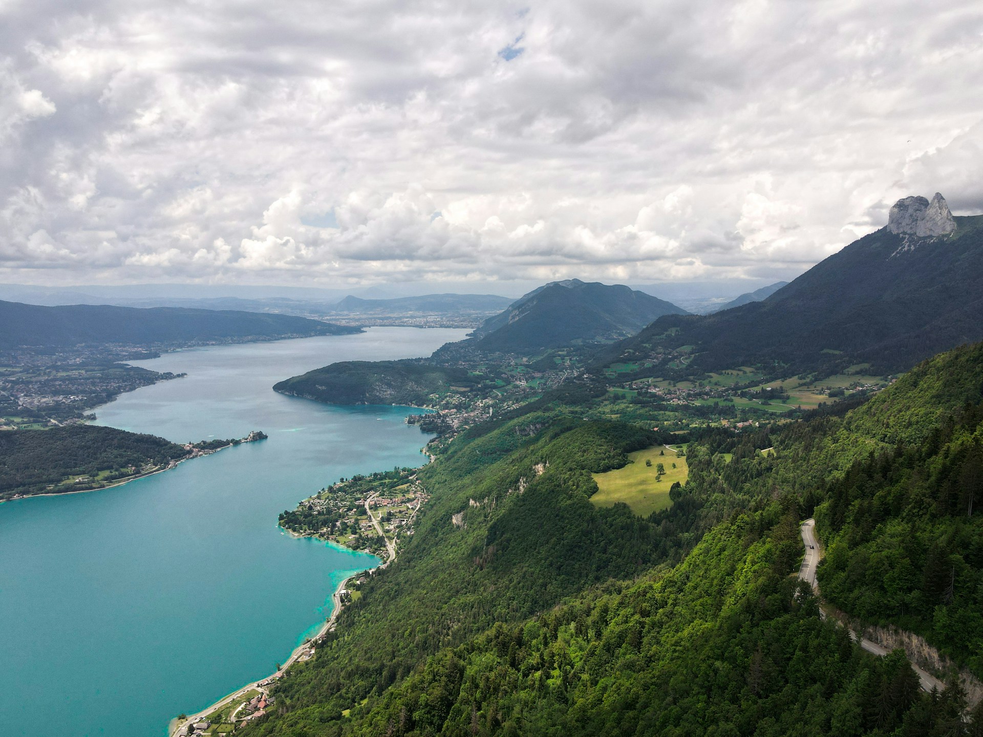 green grass covered mountain beside body of water under white clouds during daytime