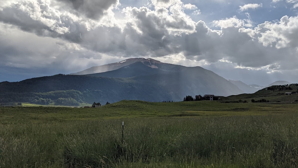 green grass field near mountain under white clouds during daytime