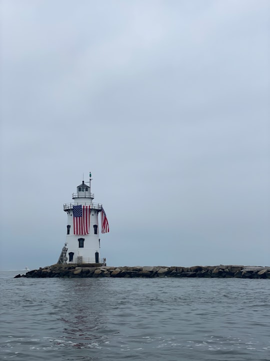 white and red lighthouse on brown rock formation near body of water during daytime in Connecticut United States