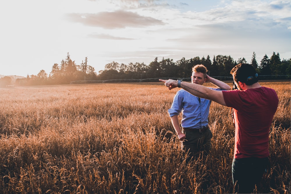 man in white t-shirt and blue denim jeans standing on brown grass field during daytime