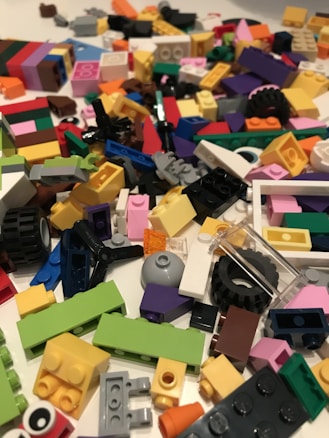 A colorful assortment of various Lego pieces scattered on a surface, including blocks, wheels, and connectors in a variety of shapes and sizes.