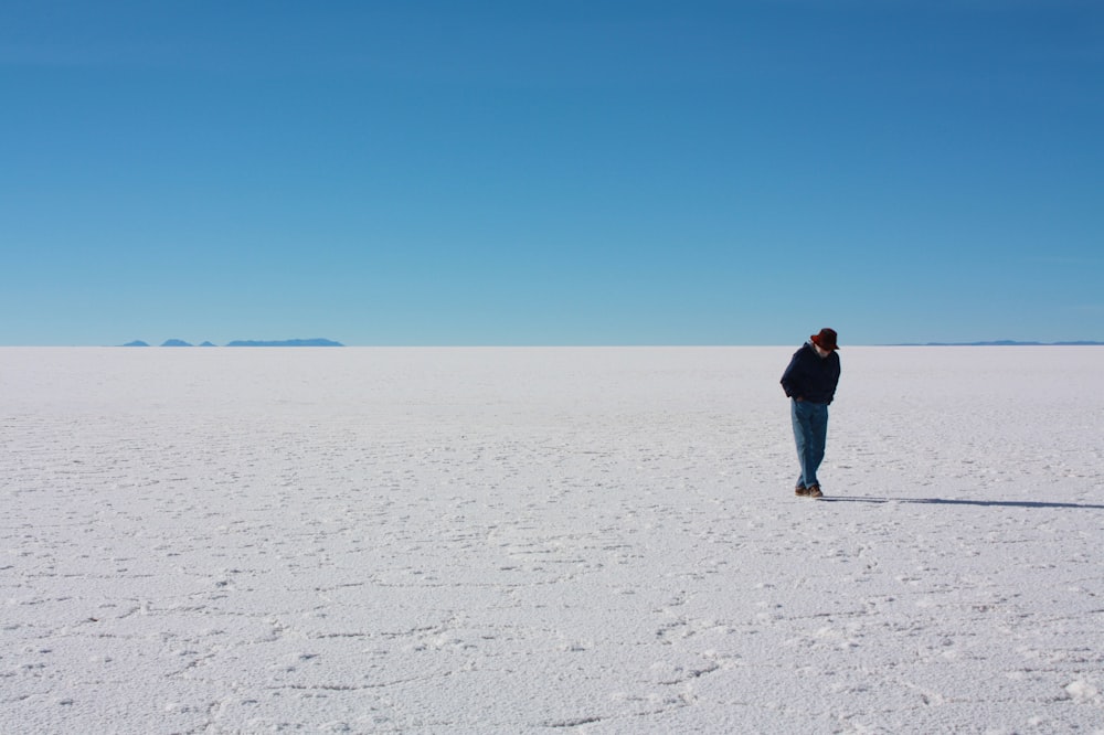 Hombre con chaqueta negra caminando sobre arena blanca durante el día