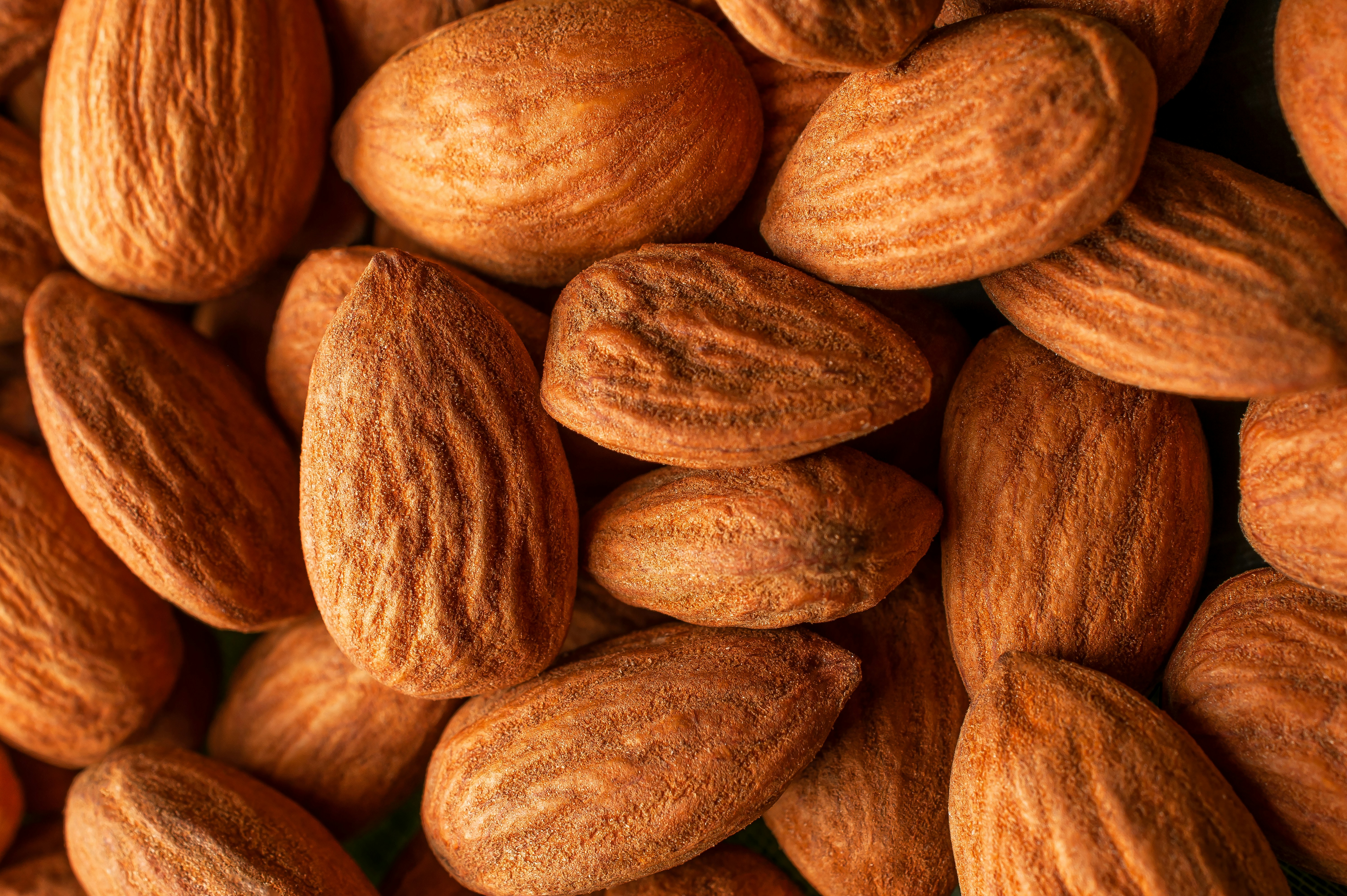 A bottle of almond oil surrounded by almonds.