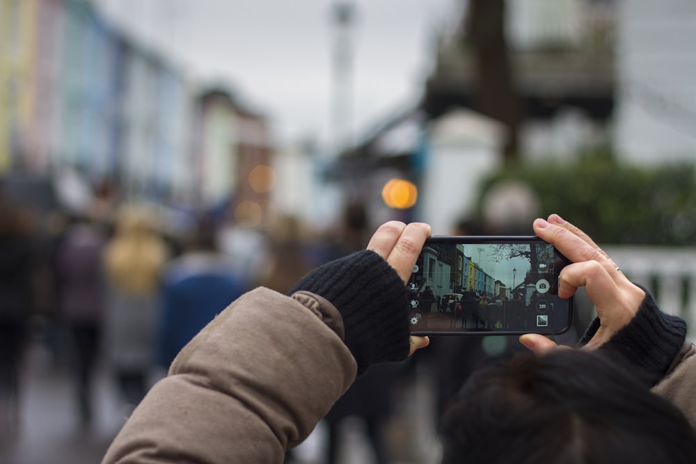 pessoa segurando smartphone preto tirando foto de pessoas durante o dia