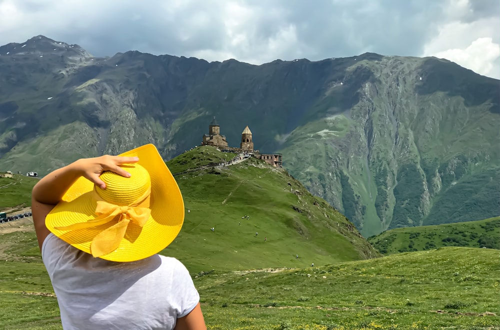 흰색 티셔츠와 노란 모자를 쓴 사람이 낮 동안 푸른 잔디밭에 서 있다