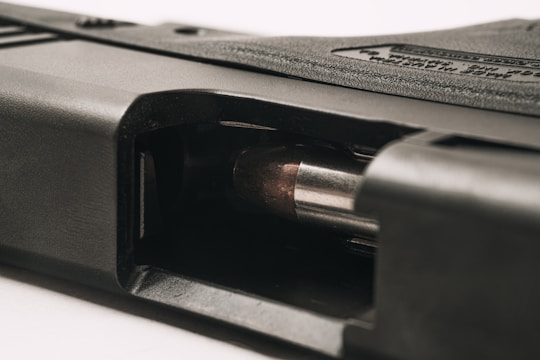 A close-up view of a firearm with a visible bullet in the chamber. The metallic surface of the bullet contrasts with the dark, textured material of the gun. The angle provides a detailed look at the mechanics of the loading area.