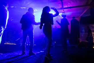 A group of friends enjoying music together, dancing with smiles under soft blue lighting.