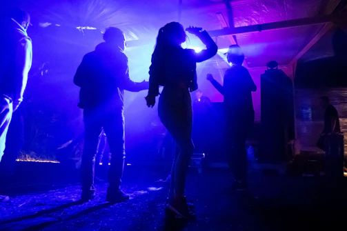 A group of friends enjoying music together, dancing with smiles under soft blue lighting.