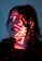 A person's face is illuminated by red light projections, possibly displaying characters or symbols. The person has closed eyes and dark hair, creating a contemplative or serene expression. The lighting casts dramatic shadows, enhancing the mysterious atmosphere.