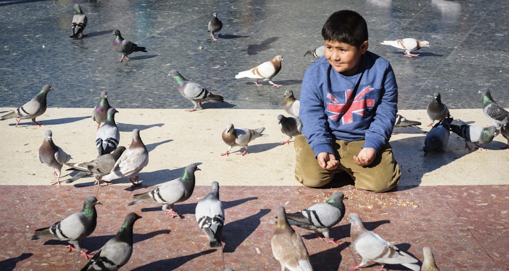 boy in blue and black jacket feeding birds