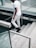 A person dressed in white is walking down a set of stone stairs, holding onto a railing. They are wearing black shoes and a dark hat outdoors.