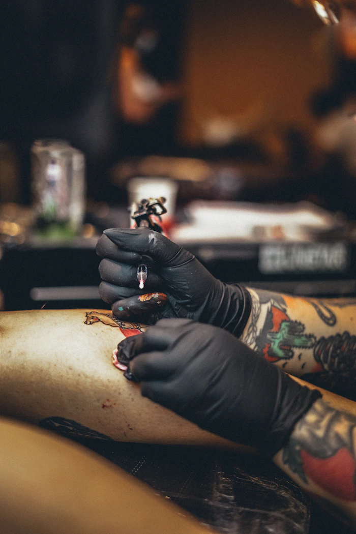 Gloved hands working on a tattoo.