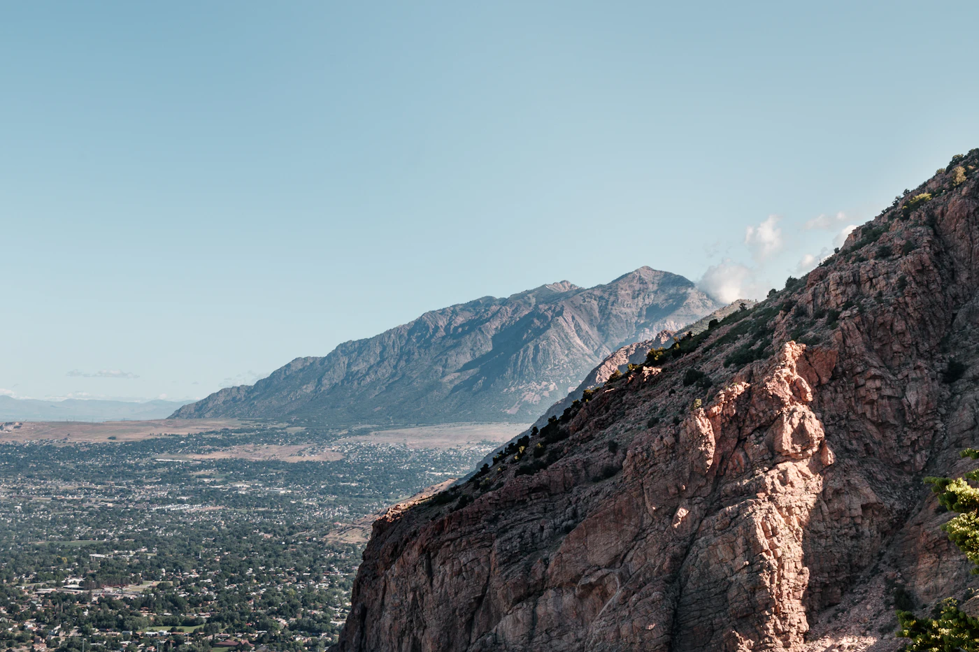 A northern Utah city spread across the valley floor beneath a steep rocky mountain face