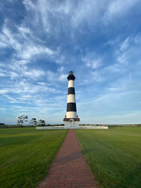 white and black lighthouse under blue sky during daytime in Cape Hatteras National Seashore United States