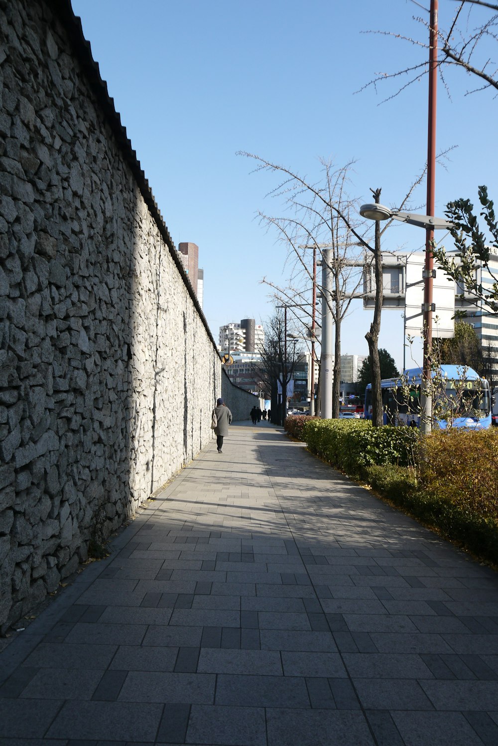 a person walking down a sidewalk next to a stone wall