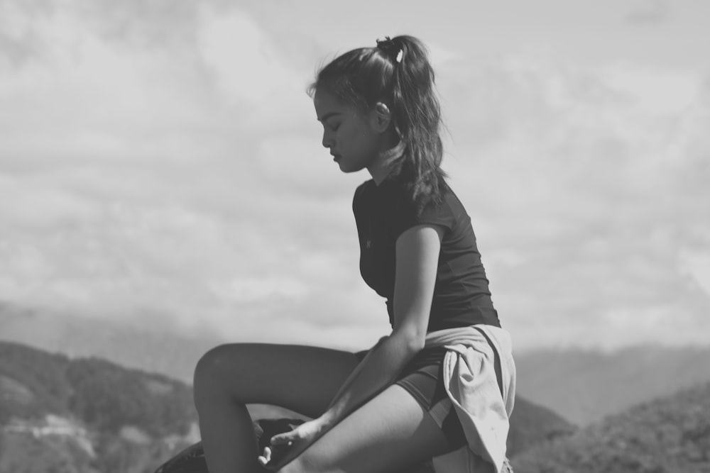 woman in black t-shirt and white skirt sitting on rock